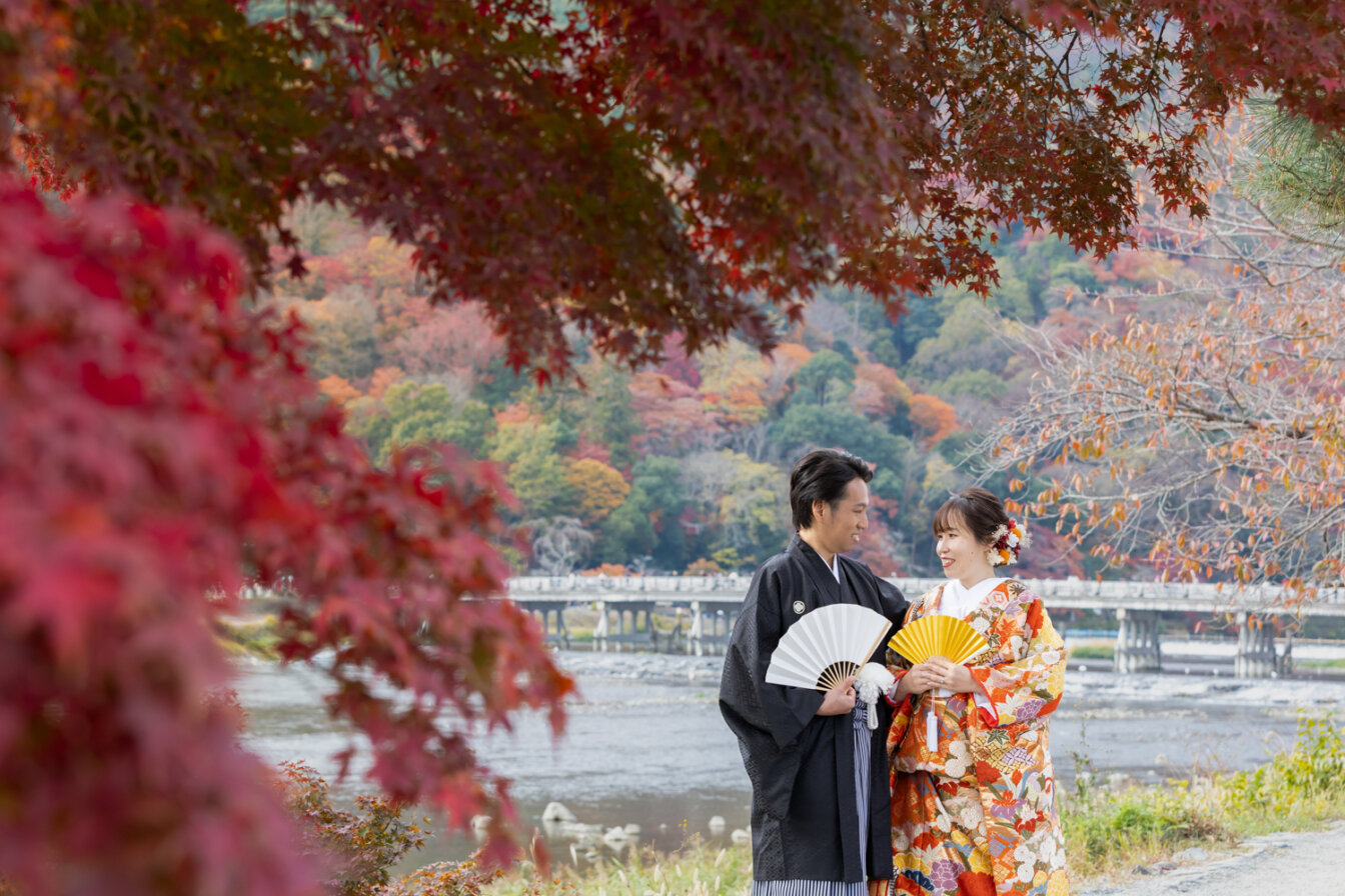 秋の嵐山で渡月橋を背景に前撮りを行う新郎新婦
