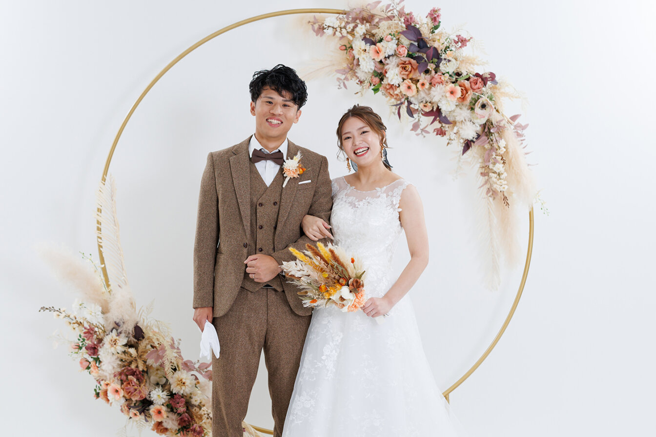 スタジオのフラワーアーチ背景で洋装前撮りを行う新郎新婦