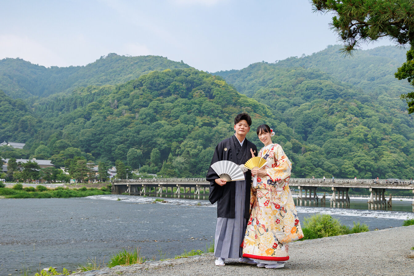 嵐山の渡月橋を背景に和装前撮りを行う新郎新婦
