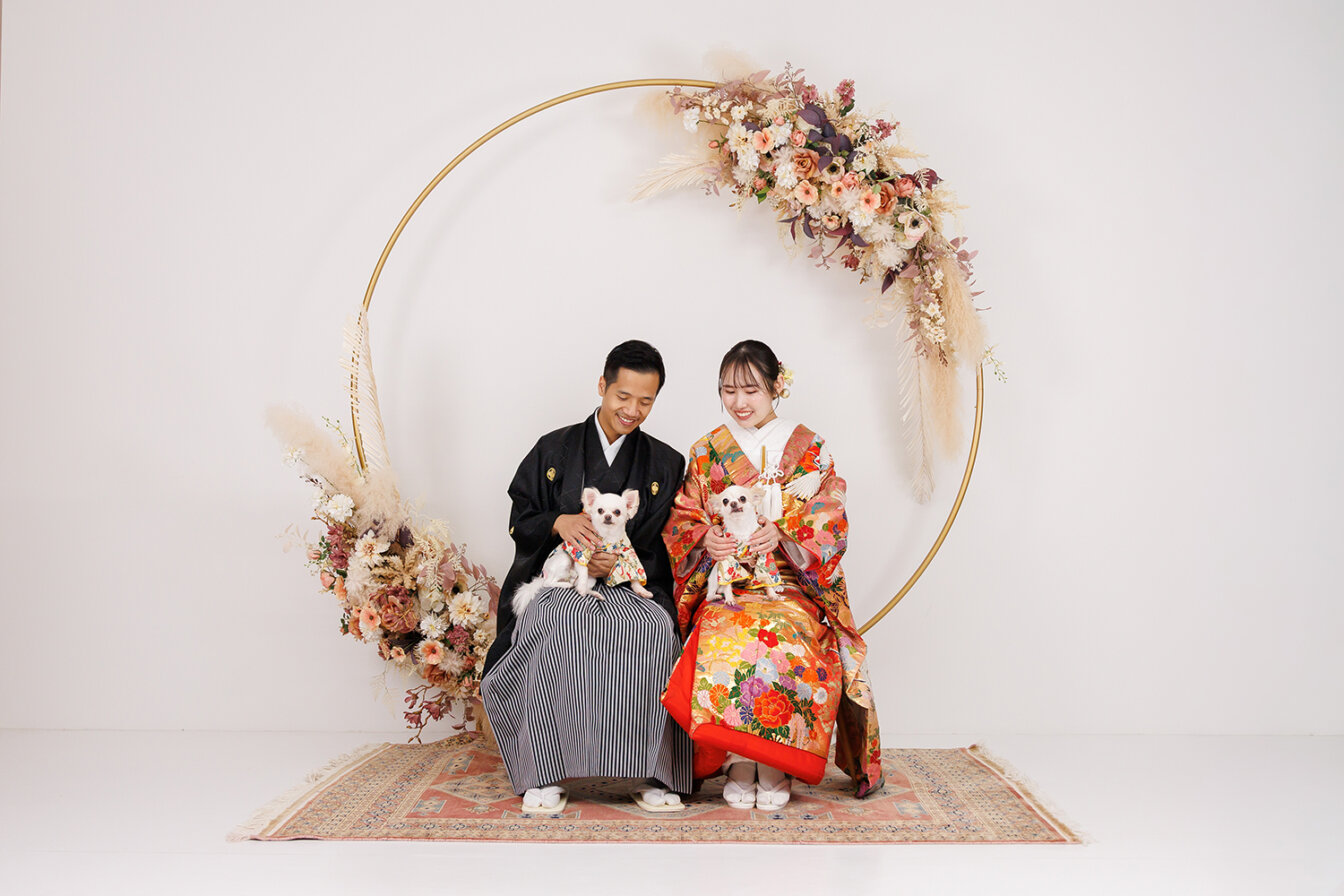フラワーアーチを背景にワンちゃんと前撮りをする新郎新婦